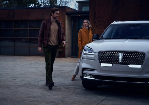 A man and a woman approaching a 2024 Lincoln Aviator® SUV, which illuminates certain lights when they are close | Allan Vigil Lincoln, Inc. in Morrow GA